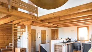 Un intérieur en bois avec un escalier, un coin cuisine et un luminaire suspendu.