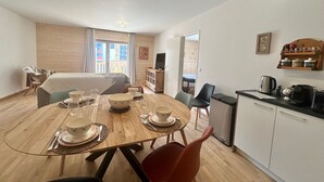 Une pièce de taille modeste comprenant une table à manger pour quatre personnes, un lit, un coin cuisine et une fenêtre donnant sur l’extérieur.