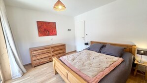 Une chambre à coucher avec un lit en bois, une table de chevet, une commode, un tableau abstrait rouge et un luminaire suspendu.