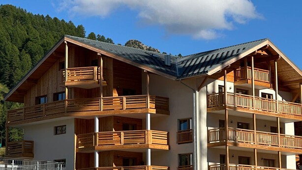 Un immeuble en bois à plusieurs étages, doté de balcons, qui se dresse sur un fond de paysage montagneux.