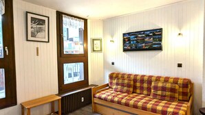 Ein gemütliches Zimmer mit einer Holzcouch, einer Holzbank und einem an der Wand befestigten Bilderrahmen.