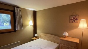 A hotel room with a bed, a nightstand, a lamp, a window with curtains, and a wall decoration.