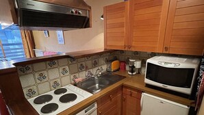 A compact kitchen with a stove, sink, microwave, and wooden cabinets.