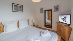 Et hotelværelse med en stor seng, et fjernsyn, et spejl og billeder i rammer på væggen.