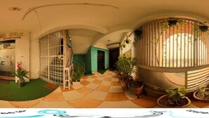 Un couloir d’hôtel avec un sol à carreaux, des plantes en pot et un espace de réception agrémenté d’une enseigne.