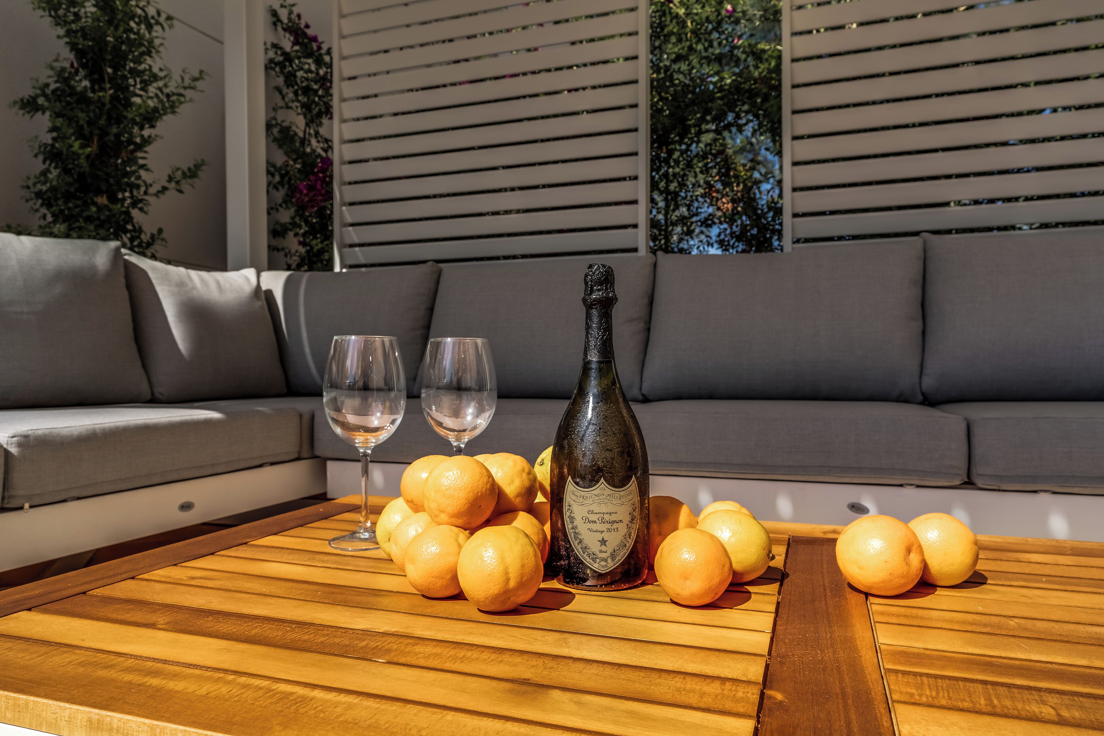 A wooden table with a bottle of champagne, two glasses, and several oranges.