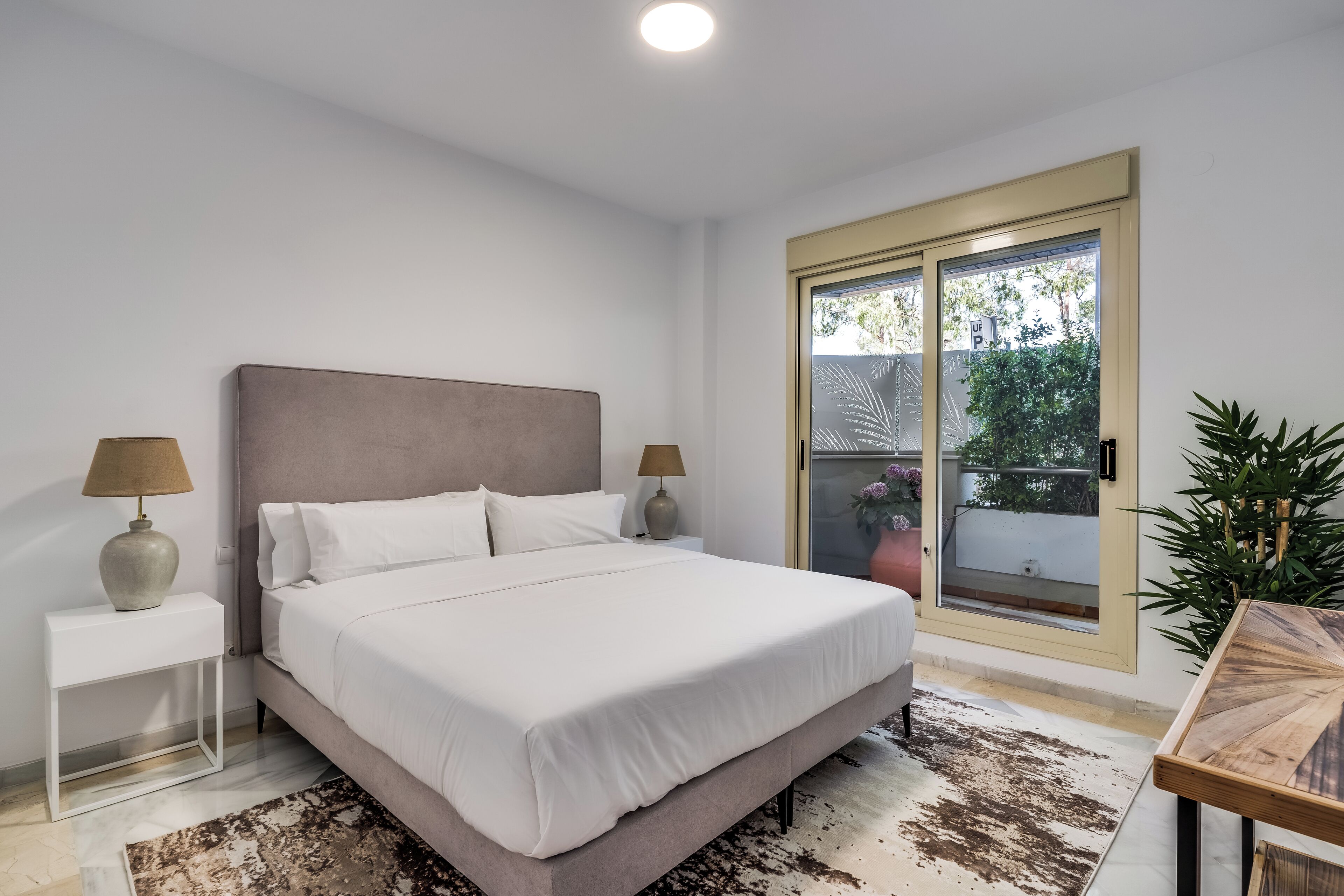 Un dormitorio con cama, mesitas de noche, una ventana y vistas al exterior.