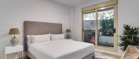 Un dormitorio con cama, mesitas de noche, una ventana y vistas al exterior.