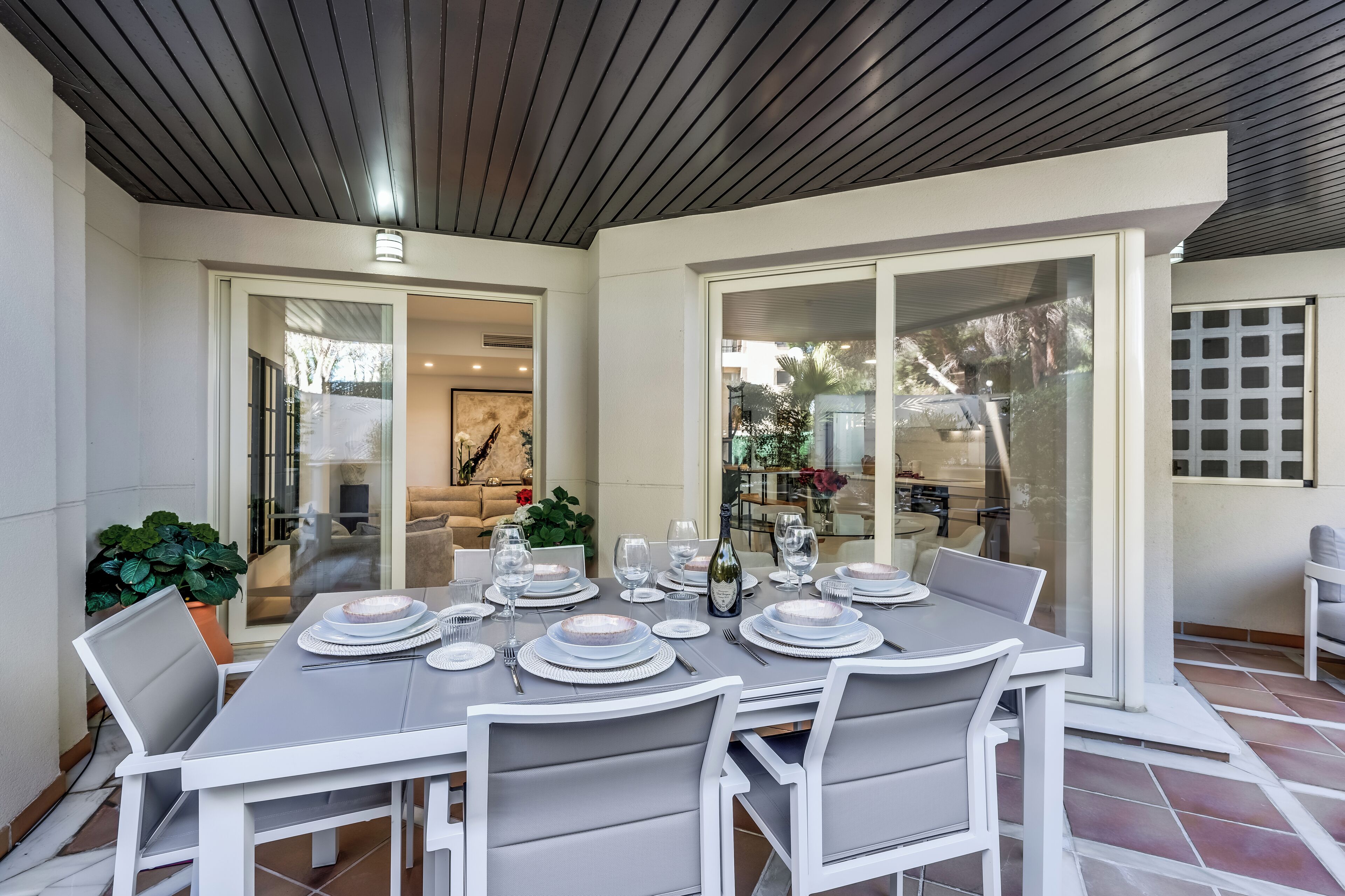 A dining area with a table set for six, surrounded by white chairs, and a glass door leading to a patio.