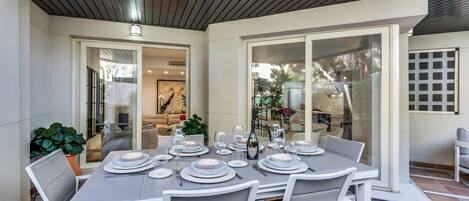 A dining area with a table set for six, surrounded by white chairs, and a glass door leading to a patio.