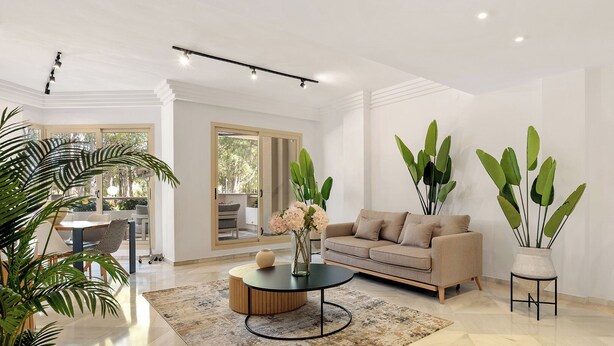 Un salon spacieux avec un canapé beige, une table basse et de grandes plantes vertes.