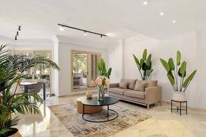 Un salón amplio con un sofá color beige, una mesa de centro y plantas verdes grandes.