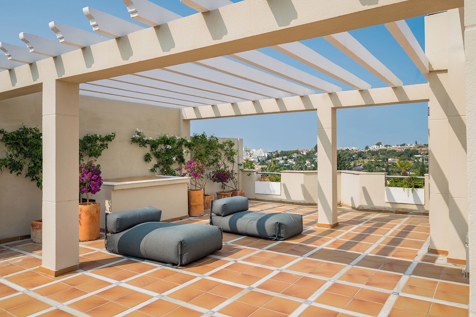A rooftop terrace with a pergola, outdoor seating, and potted plants.