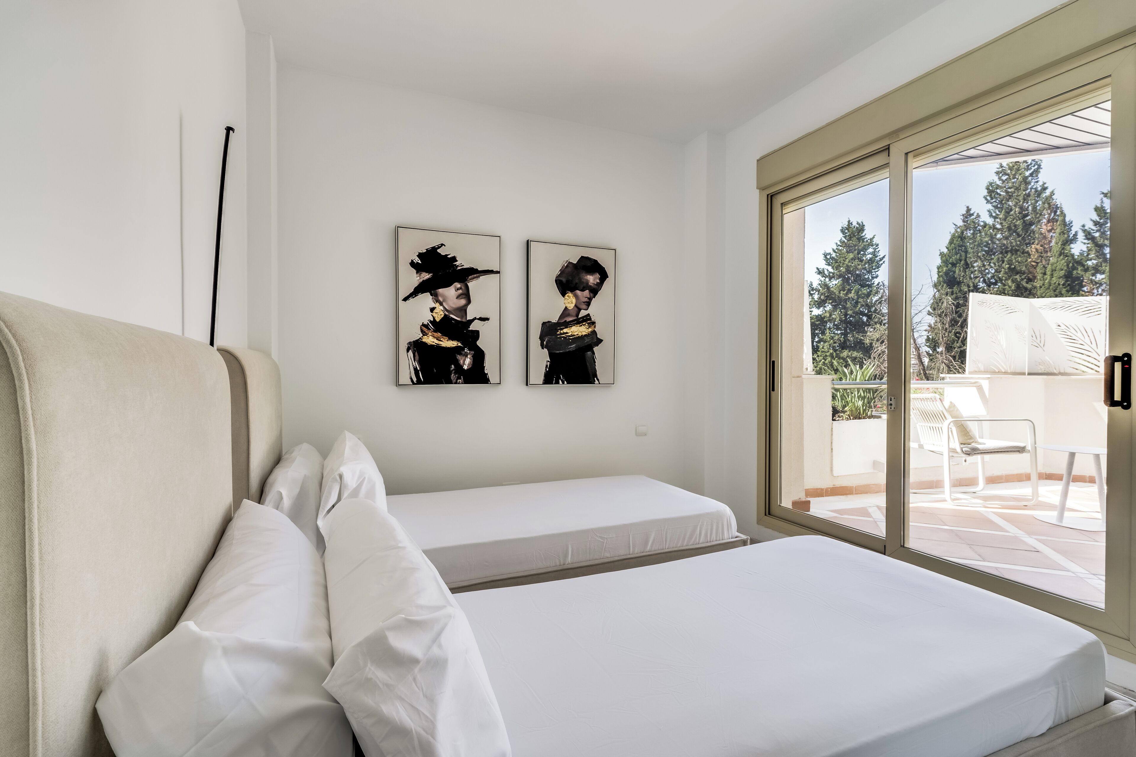 A hotel room with a bed, a sofa, and a sliding glass door leading to an outdoor area with a chair and a table.