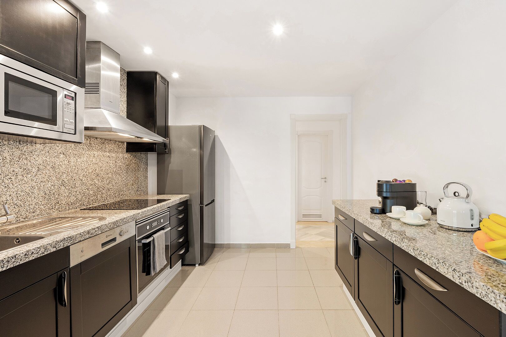 Eine moderne Küche mit Granit-Arbeitsplatten, Edelstahlgeräten und einer weißen Tür im Hintergrund.