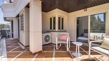 Une terrasse extérieure couverte, dotée d’un sol carrelé, d’une chaise blanche, d’une petite table et d’un canapé.
