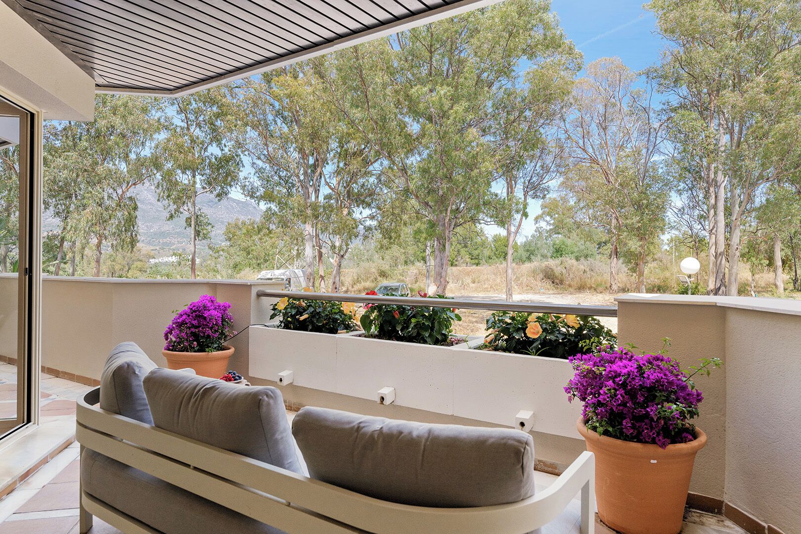 A balcony with a sofa, potted plants, and a view of trees and mountains.