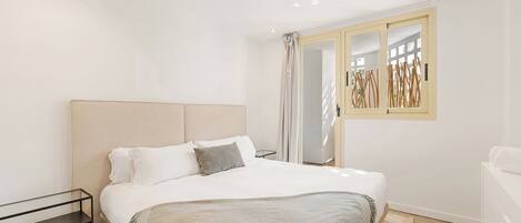 A modern bedroom with a large bed, a bedside table, and a window with a view of the outdoors.