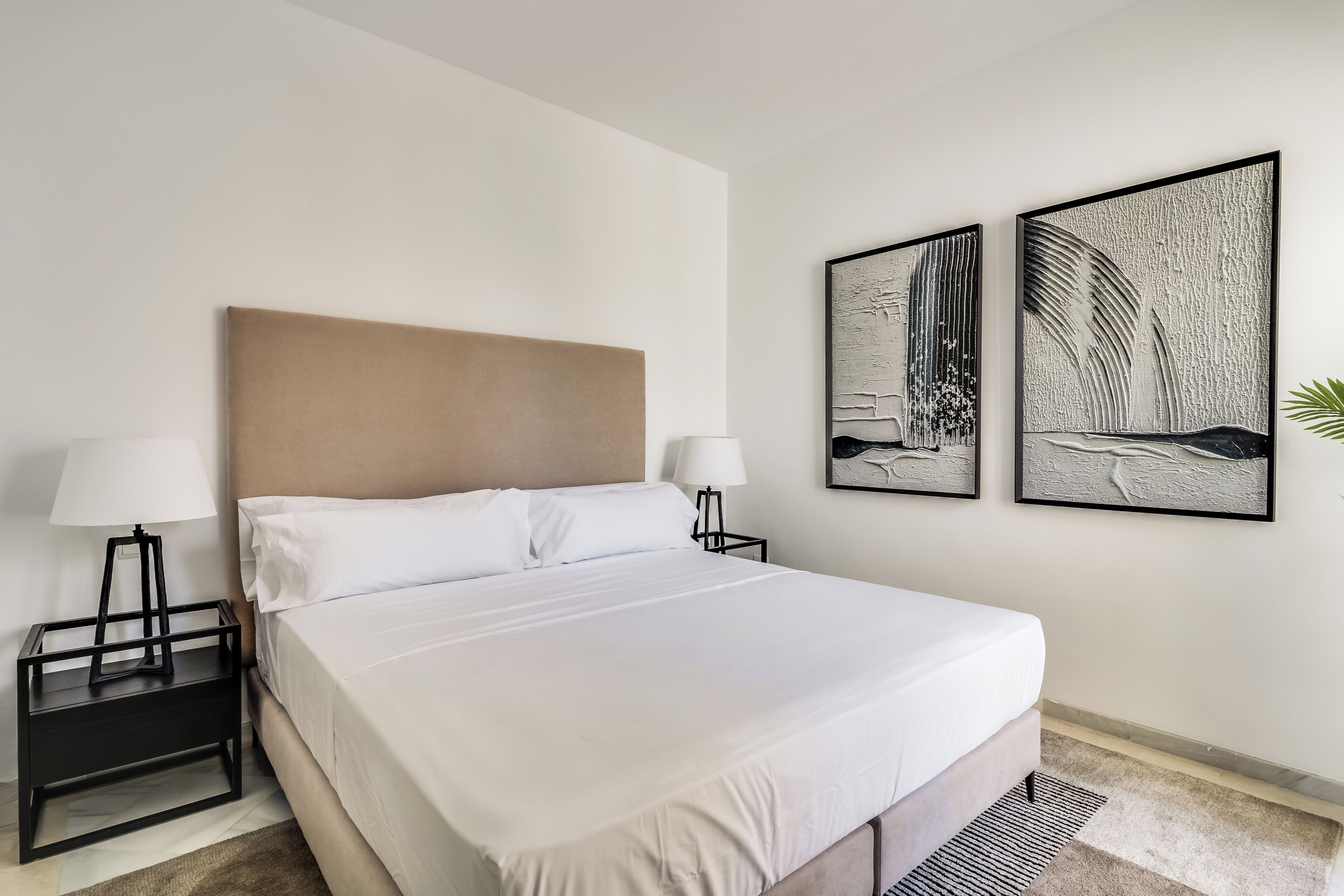 A neatly made bed with white linens, two bedside tables with lamps, and two framed artworks on the wall.