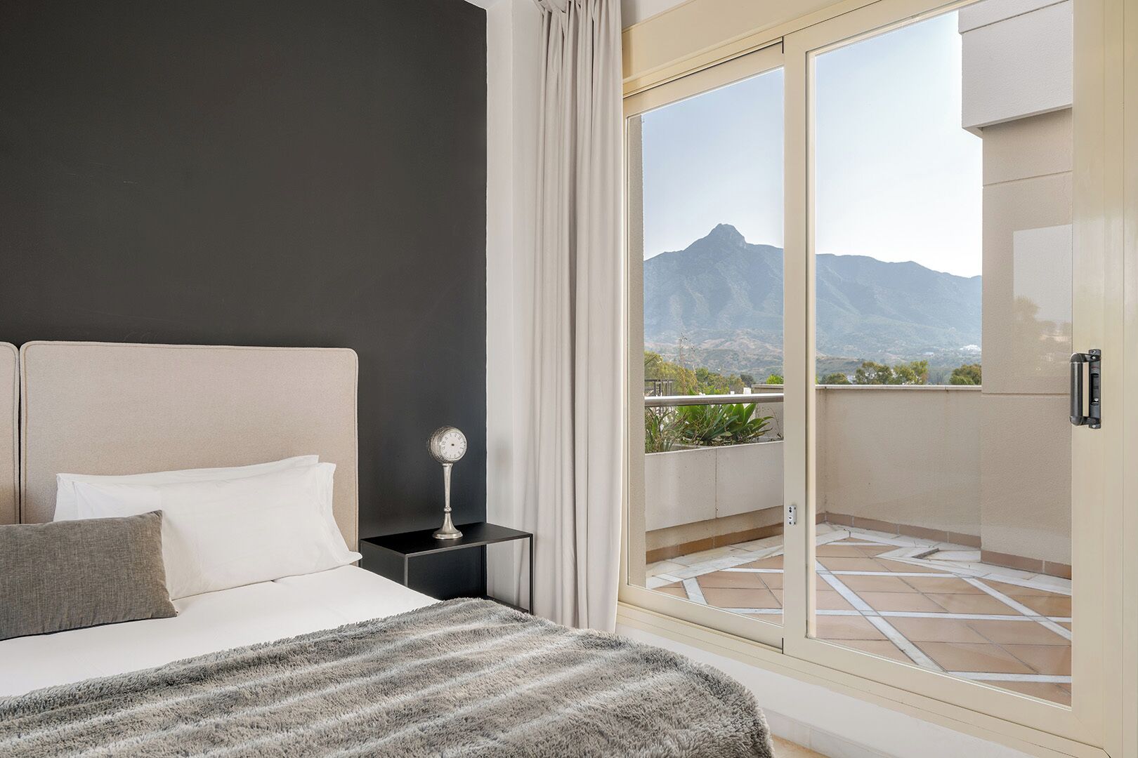 Ein Schlafzimmer mit Bett, Nachttisch und Blick auf Berge durch eine Glastür.