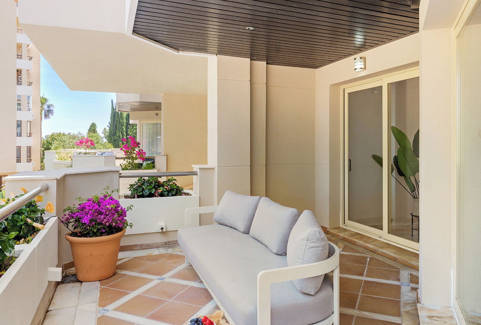 A balcony with a white sofa, potted plants, and a sliding glass door.