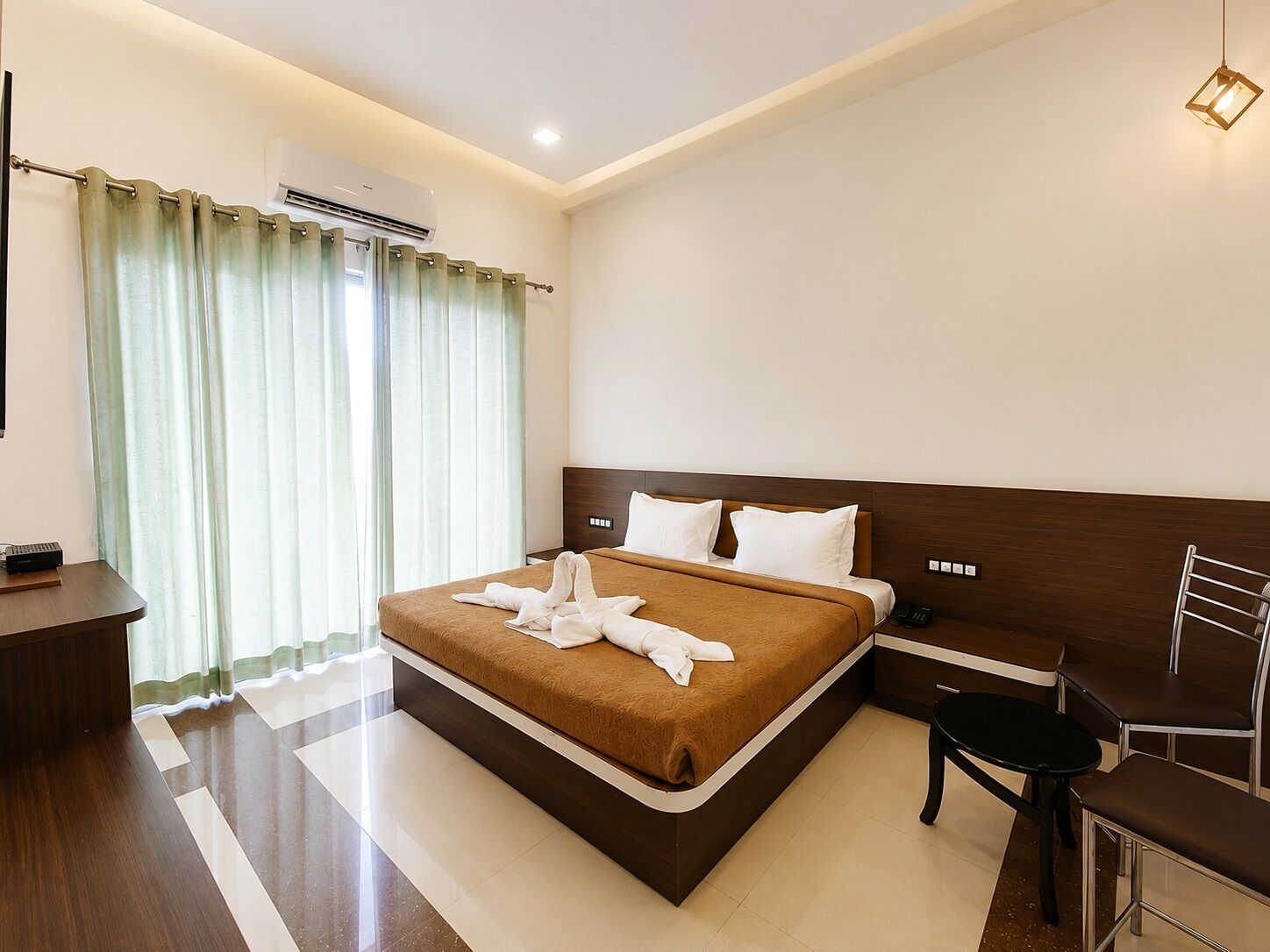 A hotel room with a large bed, a desk, a chair, and a bedside table.