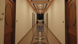 Un pasillo de hotel con suelo de estampado geométrico, puertas de madera, techo con iluminación empotrada y detalles decorativos.