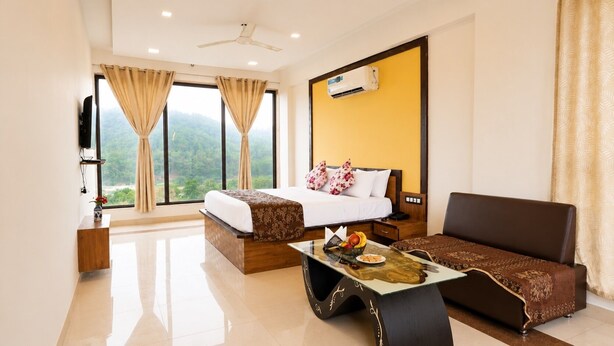 Habitación de hotel con dos camas, un sofá, un televisor, aire acondicionado y vista al exterior.