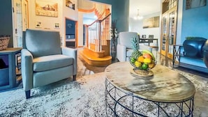 Una sala de estar con sofá, mesa de centro y frutero. Se ve una escalera que conduce a otra habitación.