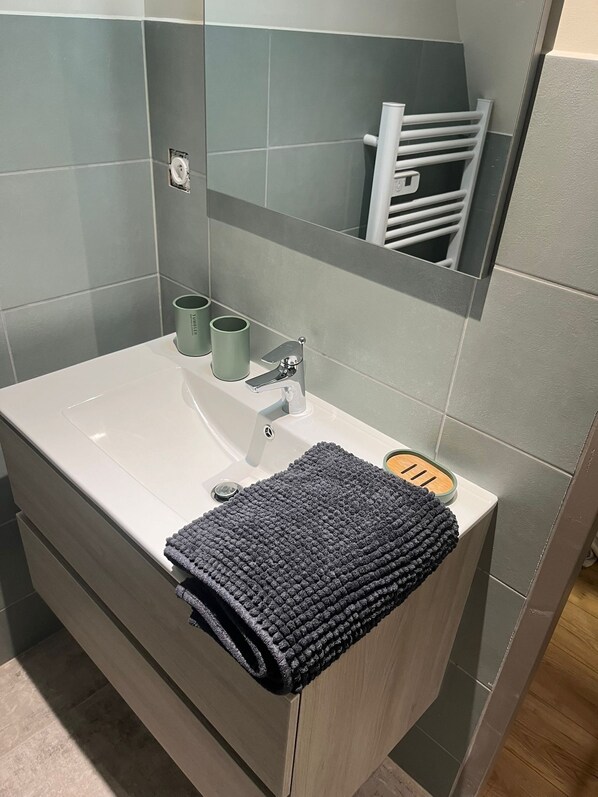 Un baño con lavamanos blanco, un espejo y un perchero para toallas.