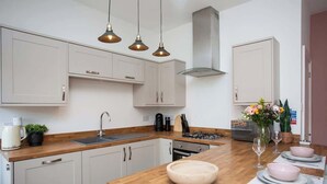 A modern kitchen with white cabinets, a wooden countertop, a gas stove, and a dining area set with plates and glasses.