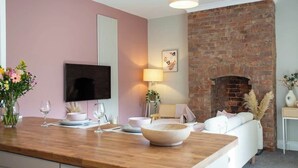 A modern kitchen with a wooden countertop, a flat-screen TV, a brick fireplace, and a white sofa.