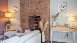A cozy room with a brick fireplace, a white sofa, a small table, and a TV on a wooden console.