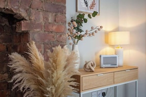 A brick wall, a white vase with dried plants, a lamp, and a small white radio on a wooden shelf.