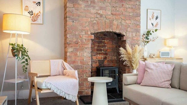 A cozy living room with a brick fireplace, a sofa, a chair, a lamp, and a small table.