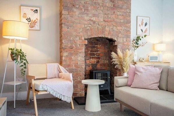 A cozy living room with a brick fireplace, a sofa, a chair, a lamp, and a small table.