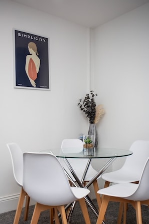 Un espace repas moderne avec une table en verre, des chaises blanches et une affiche accrochée au mur.