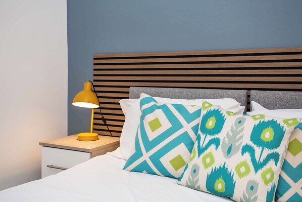 A neatly made bed with patterned pillows, a bedside lamp, and a wooden headboard.