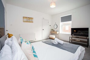 A bedroom with a bed, a bedside table, a TV, and a window.