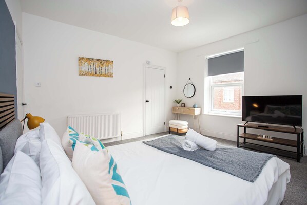 Un dormitorio con cama, mesita de noche, televisor y ventana.