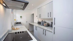 Una cocina moderna con tope de inducción negro, armarios blancos y microondas.