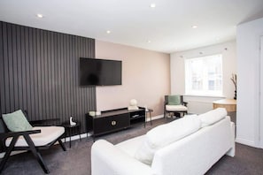 A modern living room with a flat-screen TV, a sofa, a chair, a small table, and a cabinet.