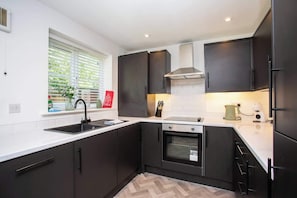 A modern kitchen with dark cabinets, a stainless steel oven, and a window with blinds.