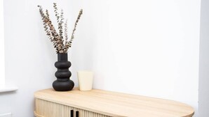 Un tavolino consolle in legno con un vaso di fiori secchi e una tazza.