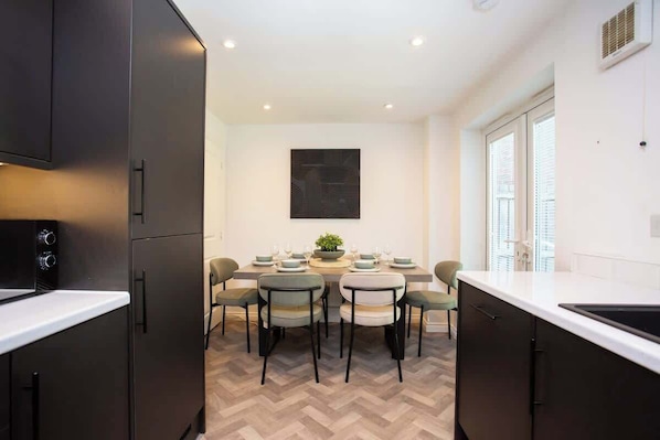 A modern kitchen with a dining area, featuring a herringbone floor pattern, a central island, and a large window.