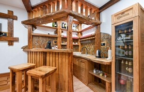 A rustic kitchen with wooden bar stools, a stone backsplash, and a Corona refrigerator.