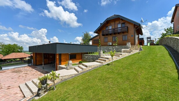 Ein zweistöckiges Holzhaus mit Balkon, einem gepflasterten Einfahrtsweg und einem Rasen.