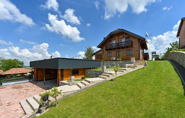 Une maison en bois à deux étages, dotée d’un balcon, d’une allée pavée et d’une pelouse verdoyante.