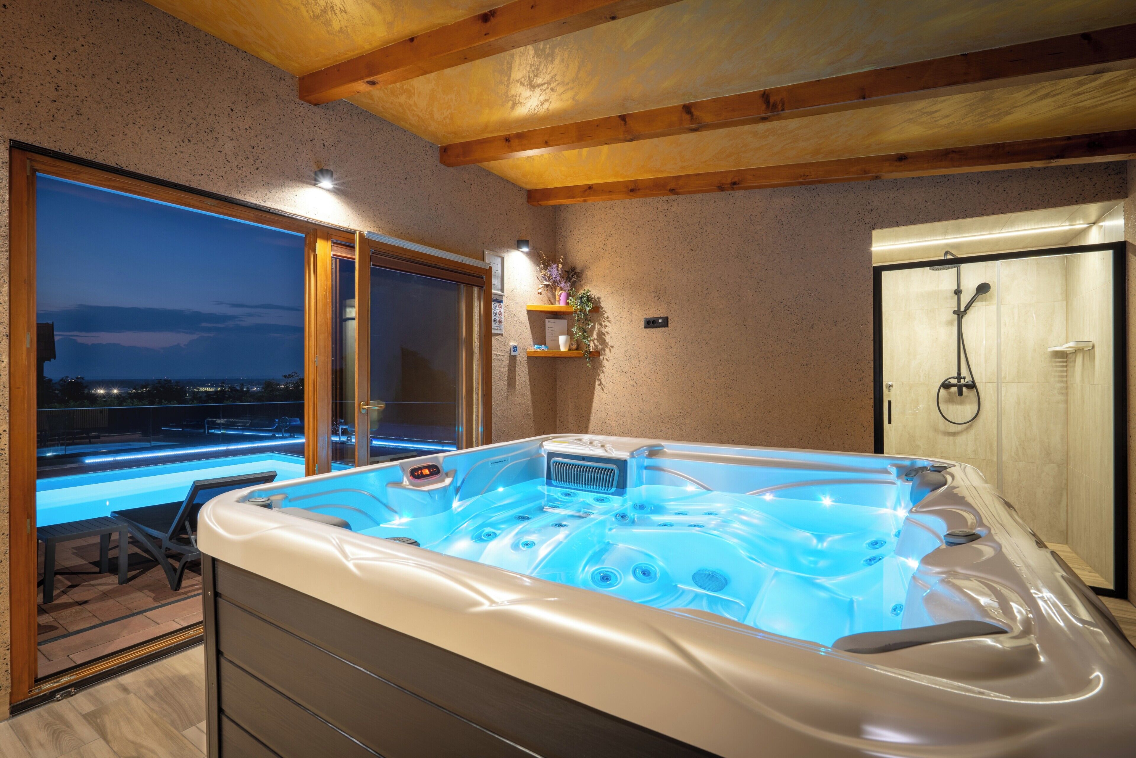 Ein Wellnessbereich mit Whirlpool, Dusche und Blick auf den Nachthimmel.