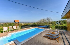 Una piscina con sillas de descanso y un muelle de madera, rodeada de una valla y árboles.